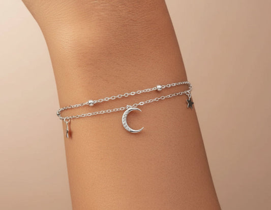 Silver anklets with moon designs on a person's ankle against a neutral background