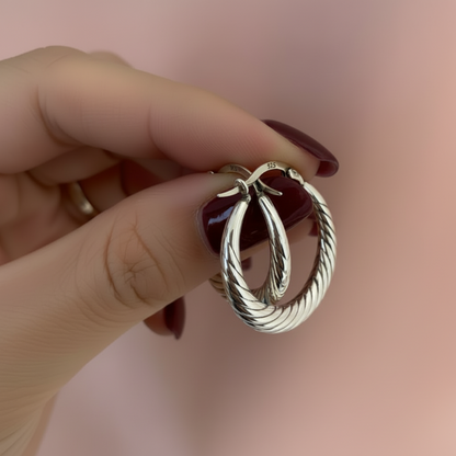 Silver hoop earrings held in a hand against a neutral background