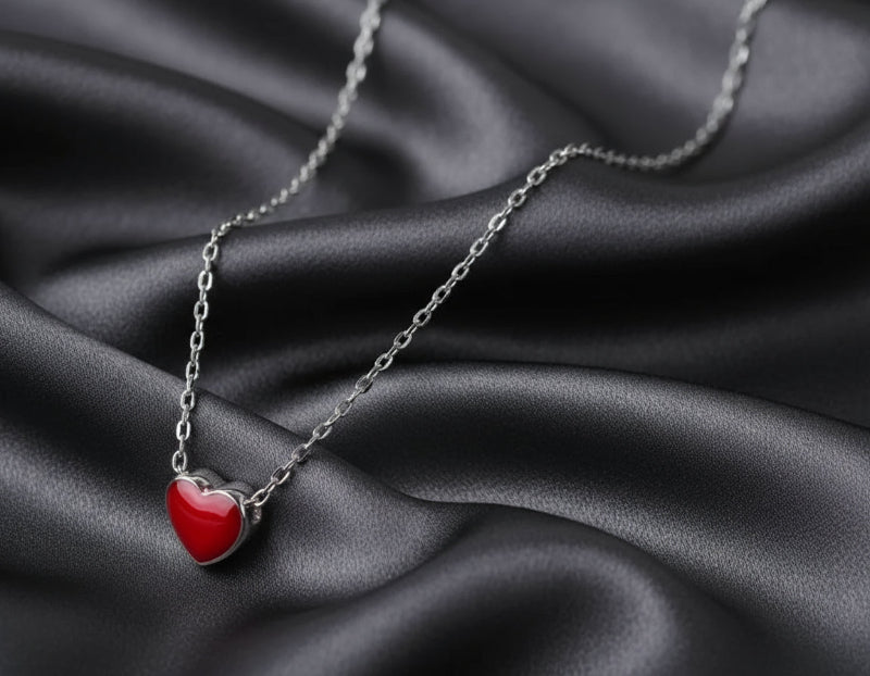 Silver necklace with a red heart pendant on a dark fabric background
