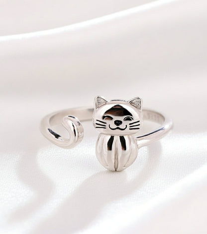 Silver cat-shaped ring on a white surface with a beige background