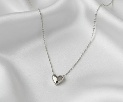 Silver heart-shaped pendant necklace on a white satin background