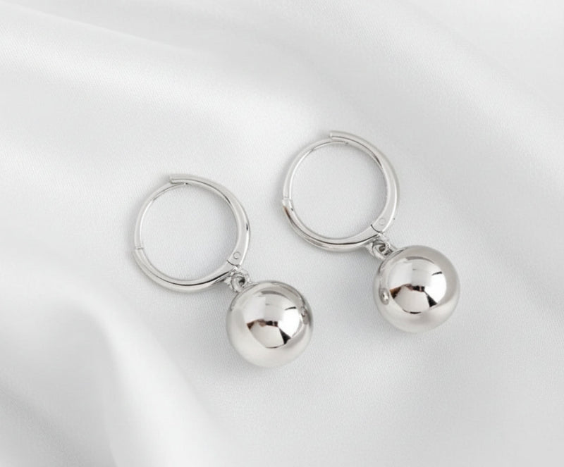 Pair of silver hoop earrings with round pendants on a white
 background