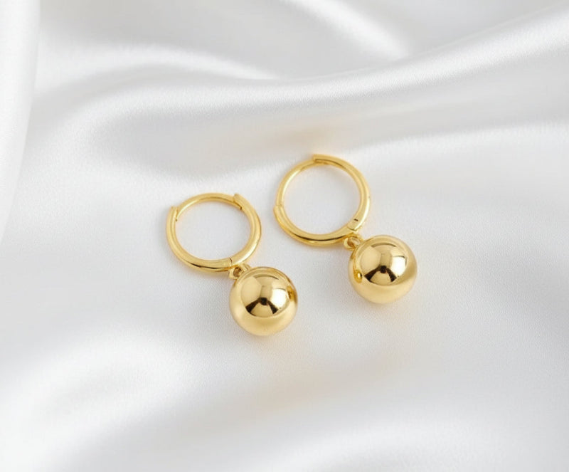 Gold hoop earrings with spherical charms on a white background