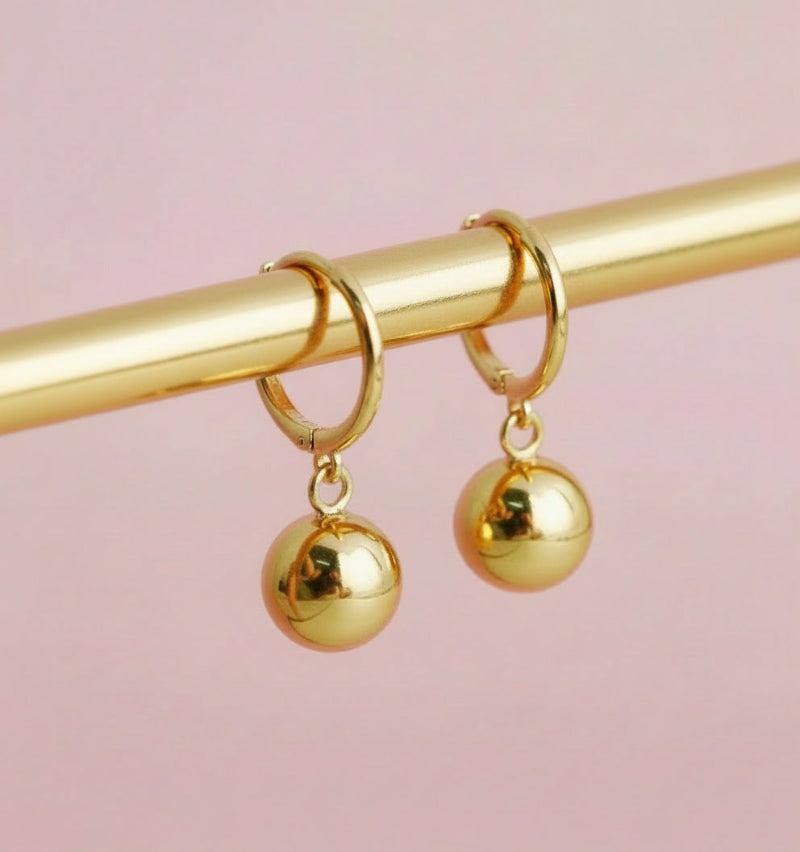 Gold hoop earrings with spherical charms on a pink background