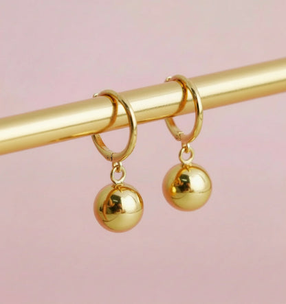 Gold hoop earrings with spherical charms on a pink background