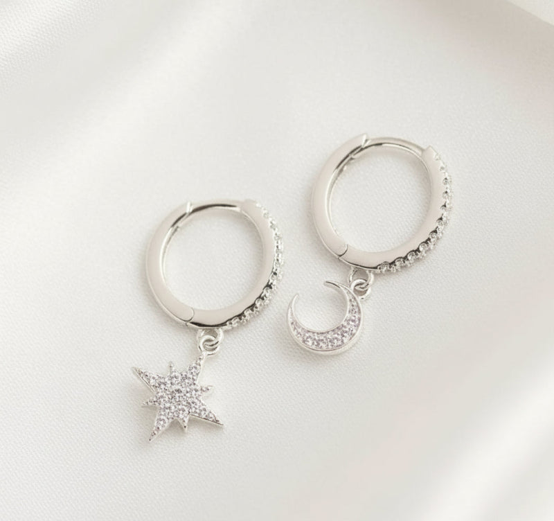 Silver hoop earrings with star and moon charms on a white background