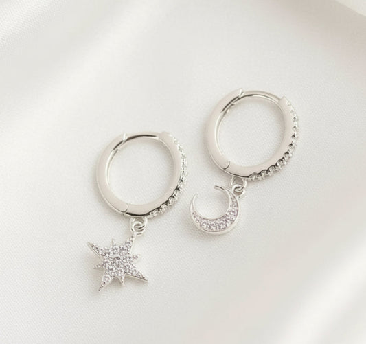 Silver hoop earrings with star and moon charms on a white background
