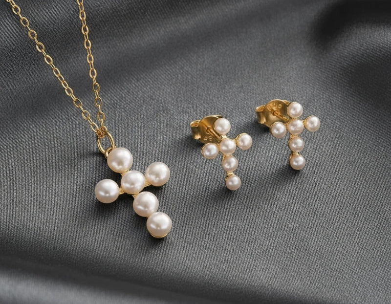 Pearl cross necklace and earrings on a pink fabric background