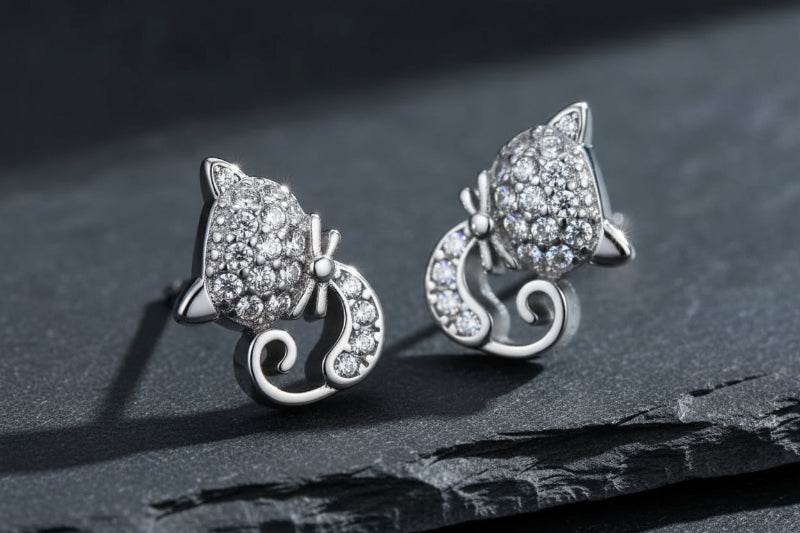 Silver cat-shaped earrings with gemstones on a green background