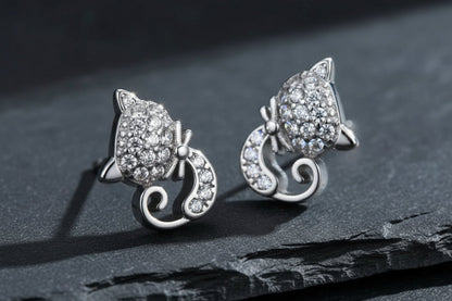 Silver cat-shaped earrings with gemstones on a green background