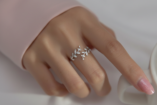 Silver ring with floral design on a finger against a neutral background