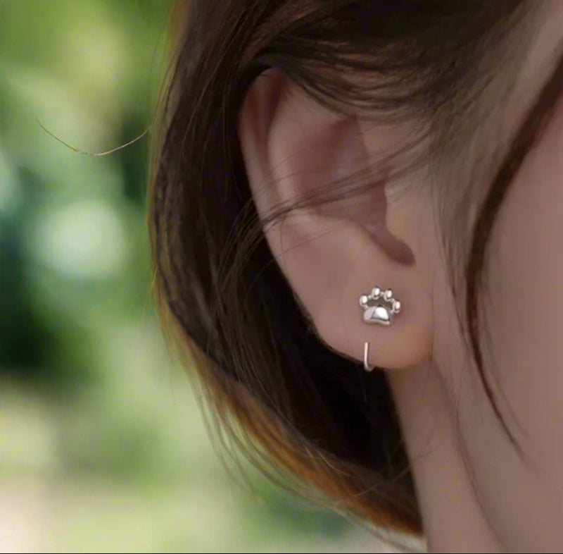 Silver paw print earring worn on an ear with a neutral background