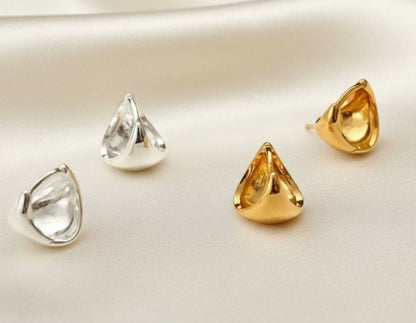 Two pairs of gold and silver teardrop-shaped earrings on a gray surface.