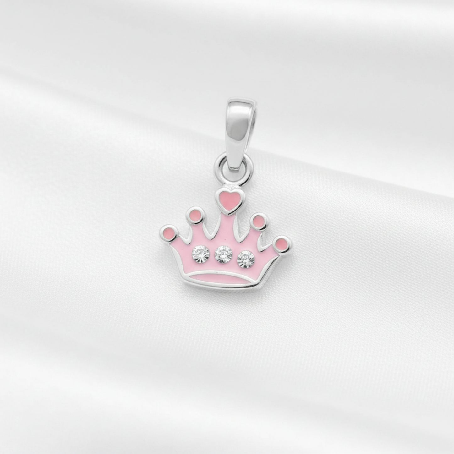 A silver crown pendant with pink enamel details and small clear rhinestones, displayed on a soft white satin fabric background.
