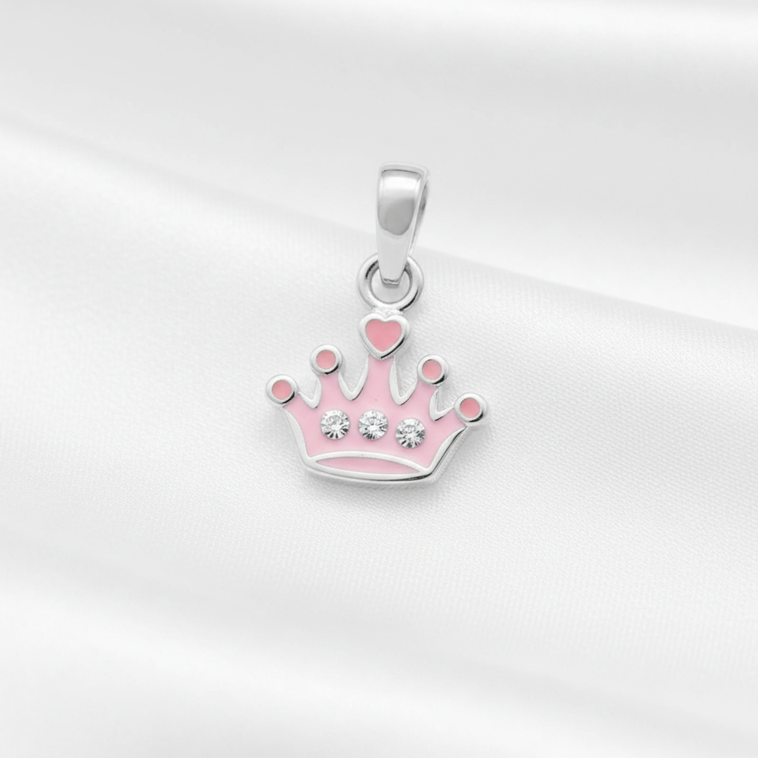 A silver crown pendant with pink enamel details and small clear rhinestones, displayed on a soft white satin fabric background.