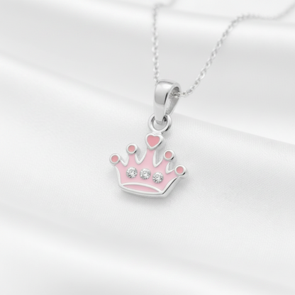 A silver crown pendant necklace with pink enamel details and small clear rhinestones, displayed on a white satin fabric background.