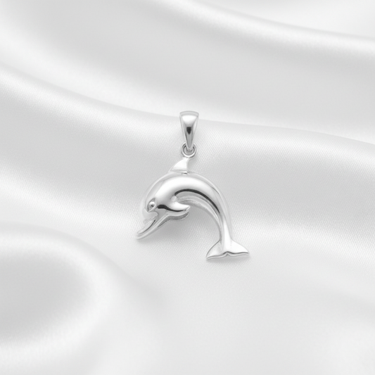 A polished silver dolphin pendant with a smooth, reflective finish, resting on a draped white satin fabric background.