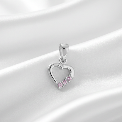 A silver heart-shaped pendant with a row of small pink gemstones along the bottom curve, displayed on draped white satin fabric.
