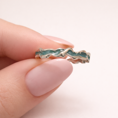 Two fingers holding silver ring with blue enamel close up/