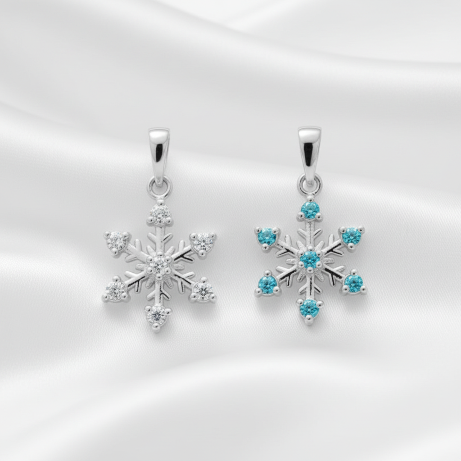 Sterling silver snowflake pendants on a white background. One is clear cubic zirconia and the other is blue cubic zirconia.