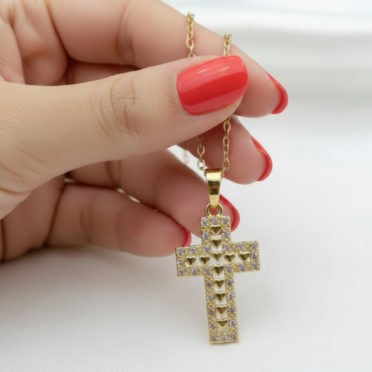 Hand with coral red nails holding gold cross pendant