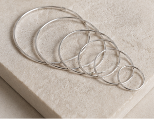 Set of silver hoop earrings on a light stone surface with a neutral background