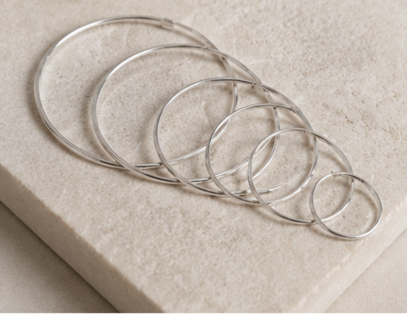 Set of silver hoop earrings on a light stone surface with a neutral background