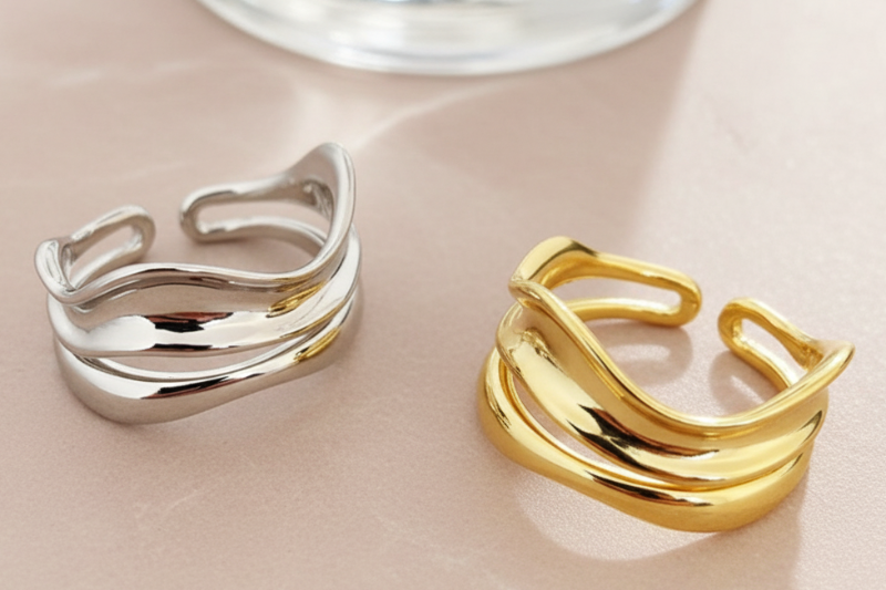 Two rings, one silver and one gold, on a marble surface with a mirror and flowers in the background.