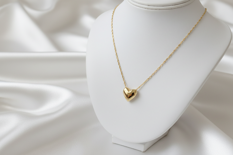 Gold heart-shaped necklace on a white mannequin bust with a soft white background