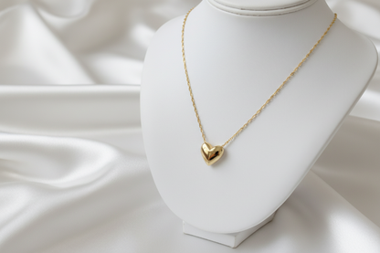 Gold heart-shaped necklace on a white mannequin bust with a soft white background