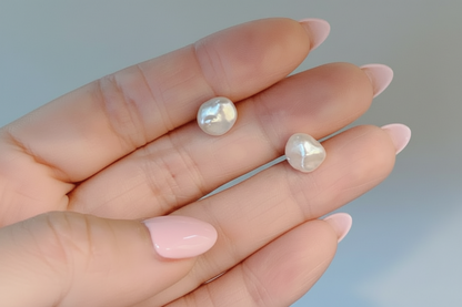 Pearl earrings held between fingers against a neutral background