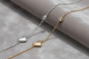 Silver bracelet with a heart charm and round gemstone on a grey fabric background