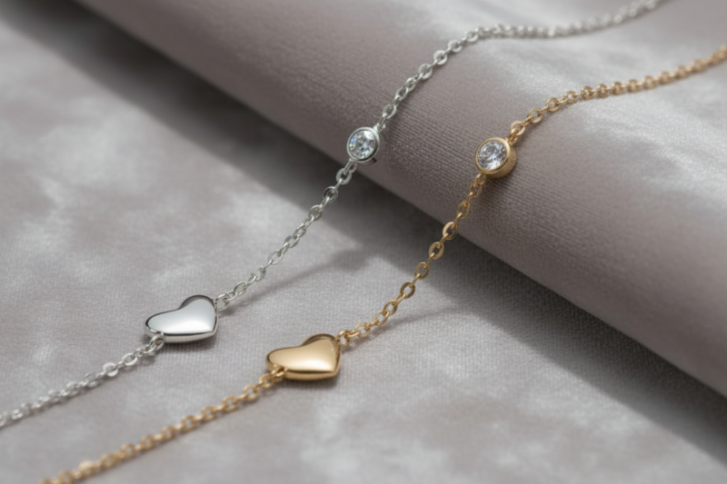 Silver bracelet with a heart charm and round gemstone on a grey fabric background