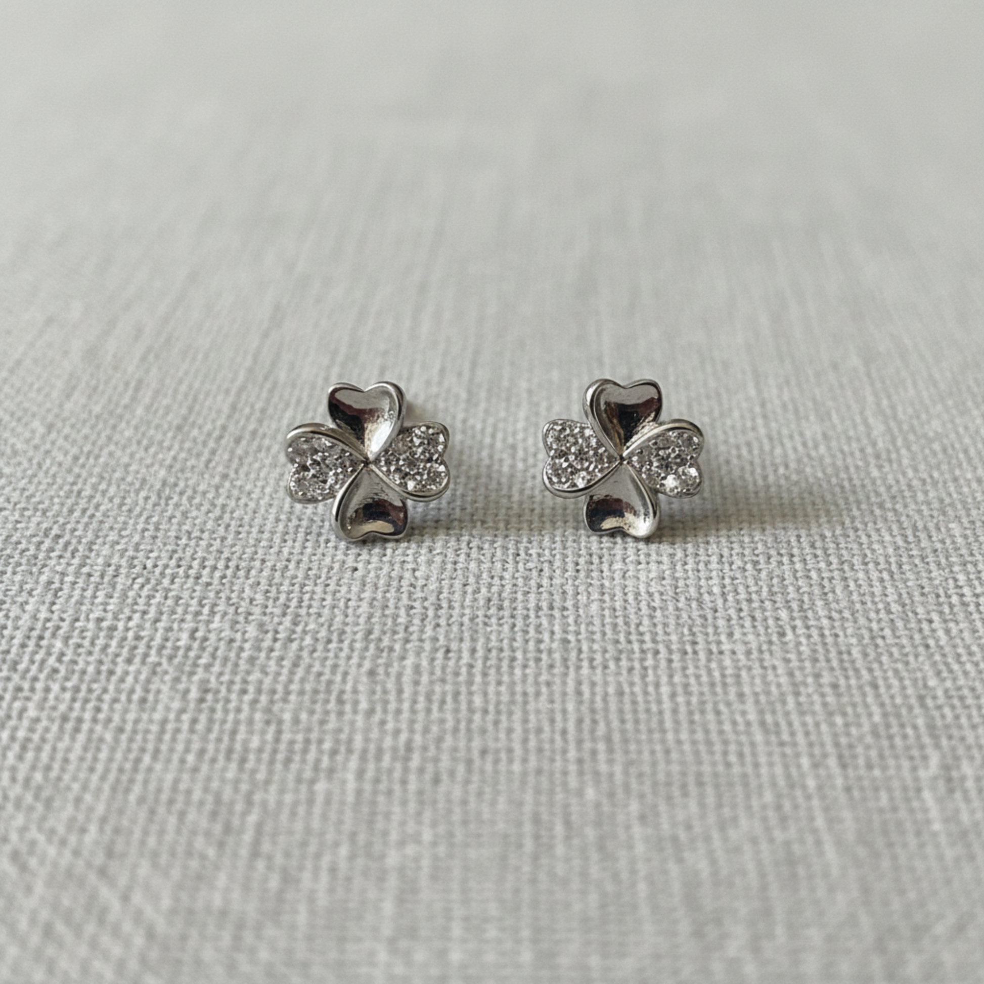 Four-Leaf Clover CZ Stud Earrings on soft grey linen background