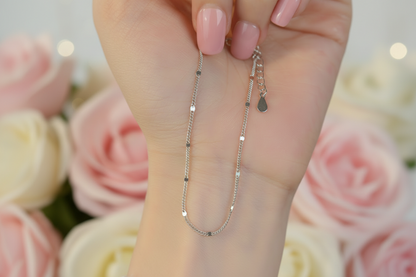 Close-up of a hand holding two delicate silver necklaces.