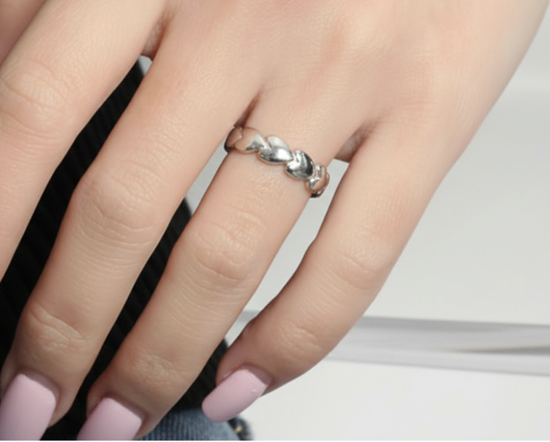Close-up of a hand wearing a heart ring, in silver, on a neutral background.