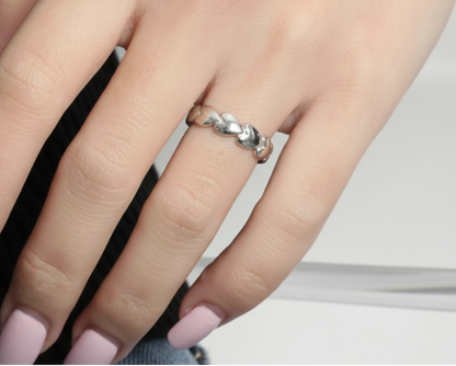 Close-up of a hand wearing a heart ring, in silver, on a neutral background.