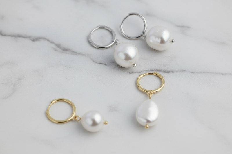 Pearl earrings with gold and silver hoops on a light gray marble background