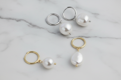 Pearl earrings with gold and silver hoops on a light gray marble background