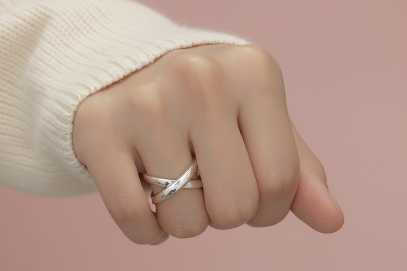 Hand wearing multiple silver rings on a neutral background