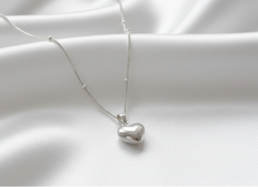 Silver heart-shaped pendant necklace on a white satin background