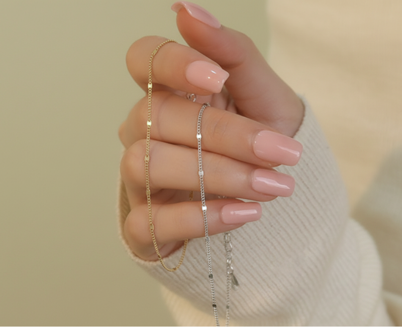 Hand wearing two delicate necklaces against a neutral background