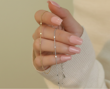 Hand wearing two delicate necklaces against a neutral background