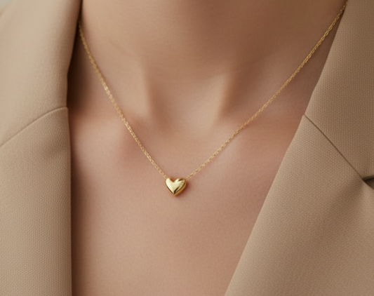 Gold heart-shaped necklace on a person's neck against a neutral background