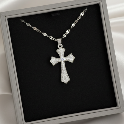 A silver cross pendant necklace with a pavé-style textured finish, displayed inside a gray presentation box with a black insert on a white satin background.