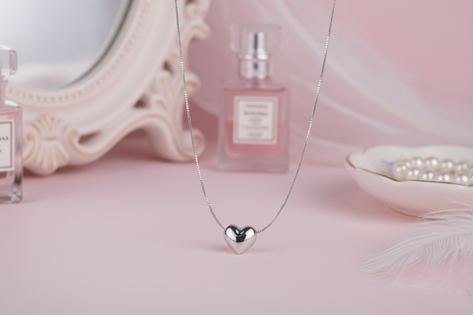 Silver heart-shaped pendant necklace on a light surface with a white dish in the background.