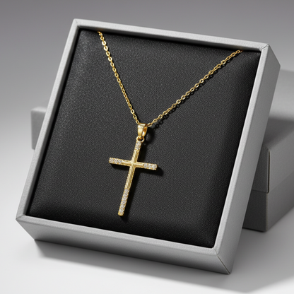 A gold cross pendant necklace with small clear stones set along the arms, displayed on a grey jewelry box.