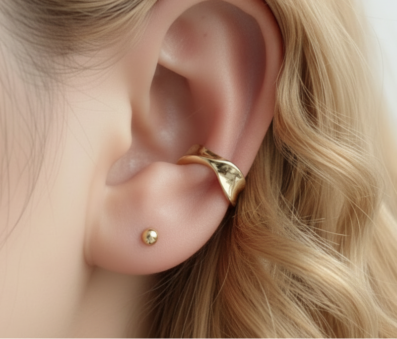 Gold earring worn on an ear with a blurred background
