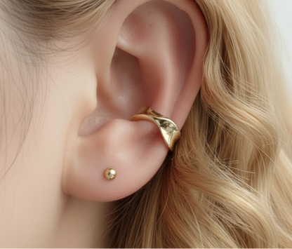 Gold earring worn on an ear with a blurred background