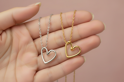 Gold and silver heart-shaped necklaces held in a hand against a beige background